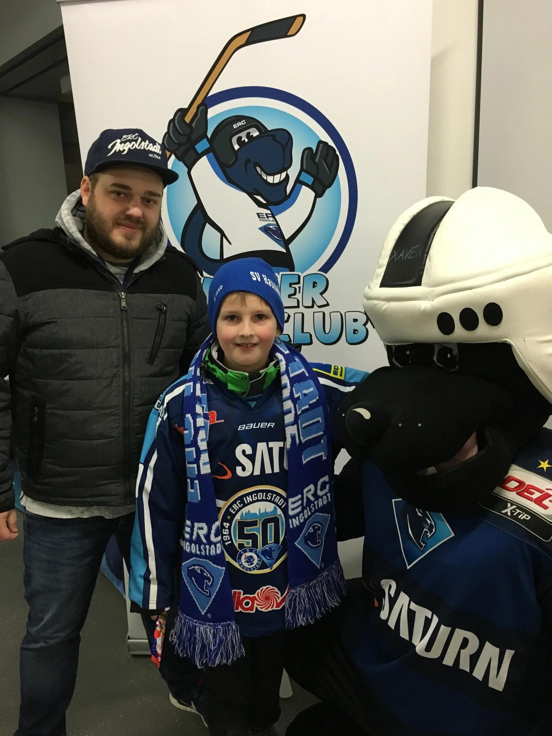Sebastian Ernhofer(Mitte) ist das 100. Mitglied des Xaver Kids-Club. Leiter Christian Müller und Maskottchen Xaver gratulieren ihm.